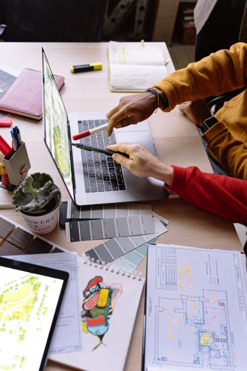 High-angle photograph of designers collaborating around a laptop with colour swatches and printed plans on the desk.
