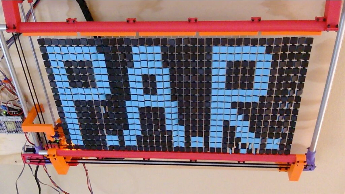 Zimm’s real P.A.R. robot beside the physical pixel-art wall it operates.