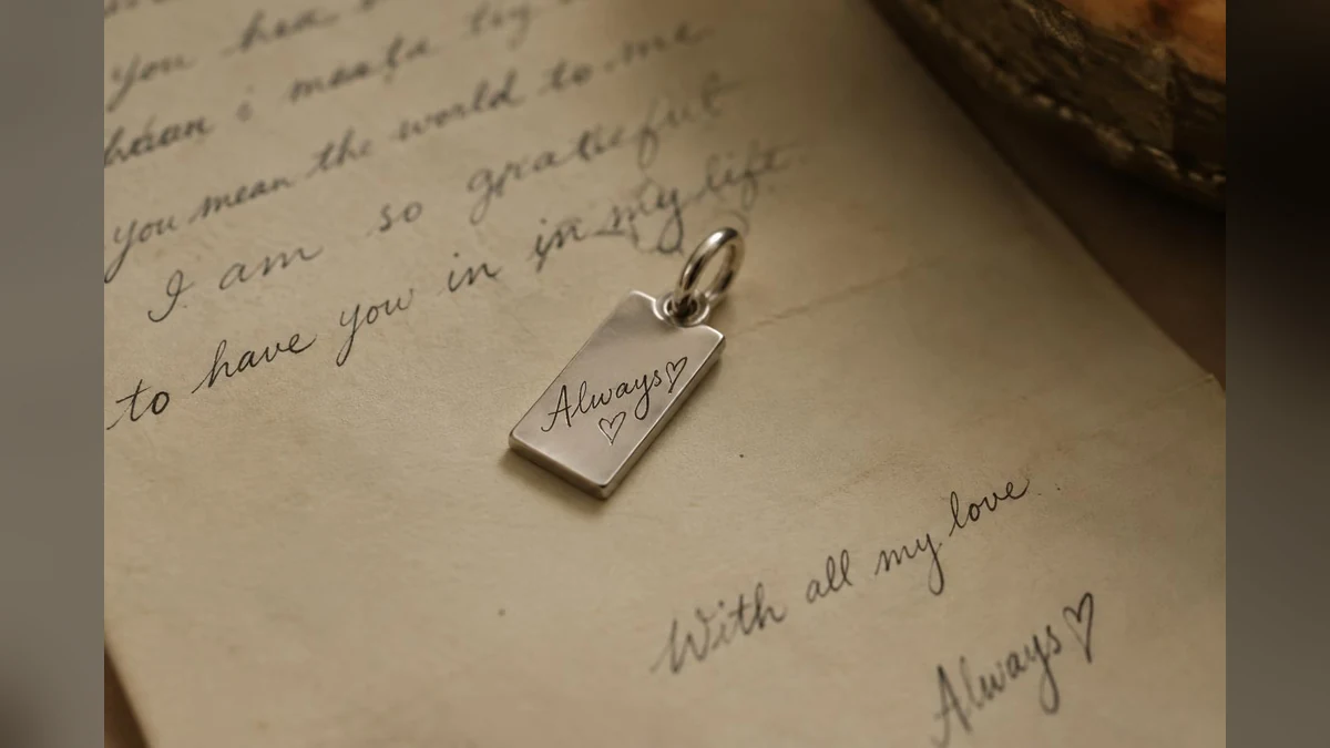 Silver pendant engraved with handwriting resting on an old letter.